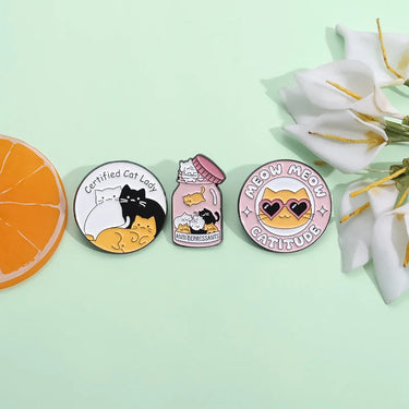Three colorful KittyNook Cat Co. Cat Lady Brooches with a slice of orange and white flowers on light green.